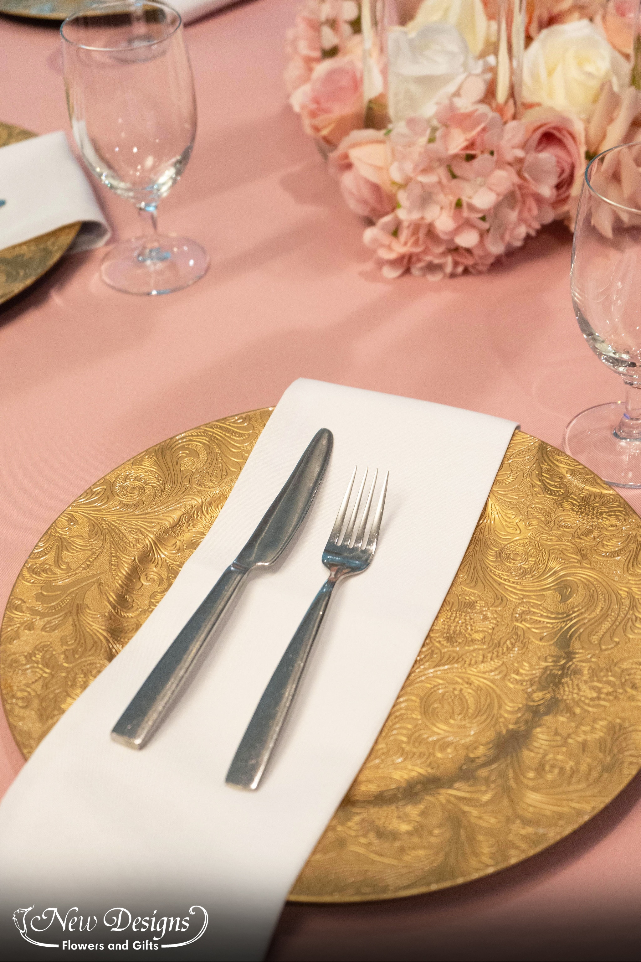 A table setting against a dusty pink tablecloth, with an ornate gold charger plate